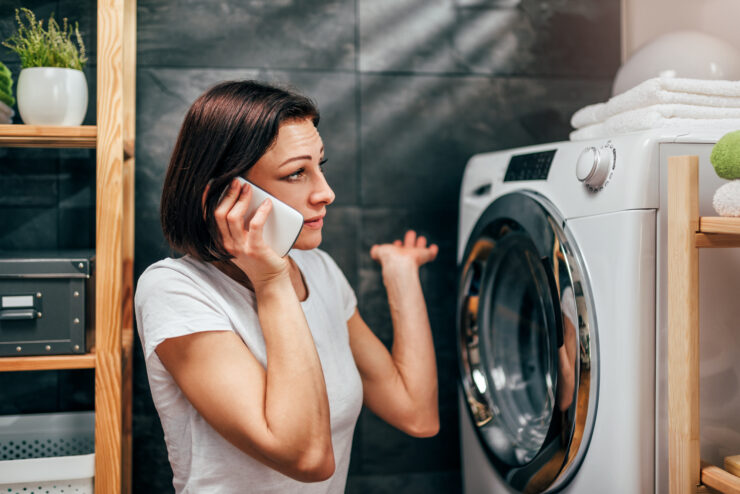 Woman wearing white shirt sitting at landry room by the dryer machine and calling for dryer repair service