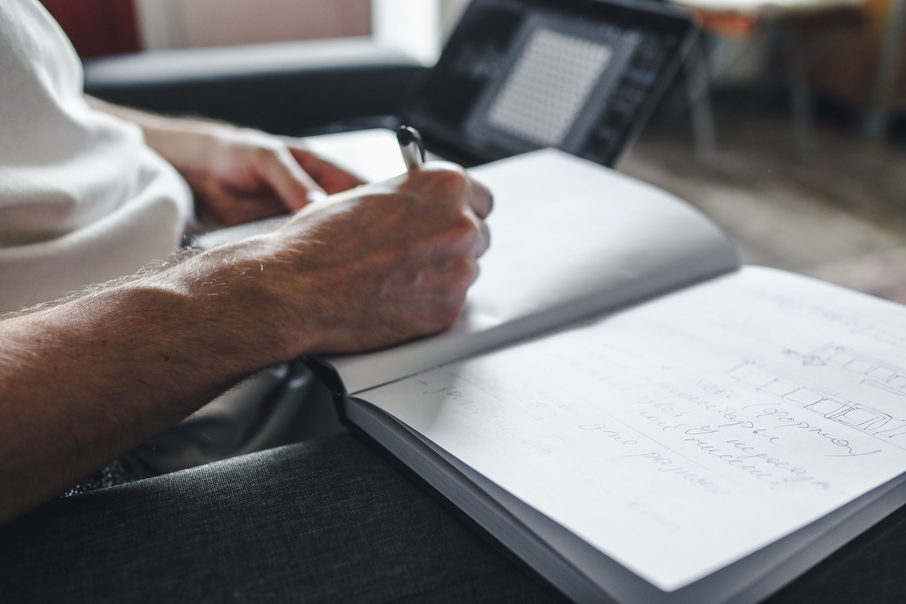 Person handwriting notes in a notebook beside a laptop, comparing human and AI writing