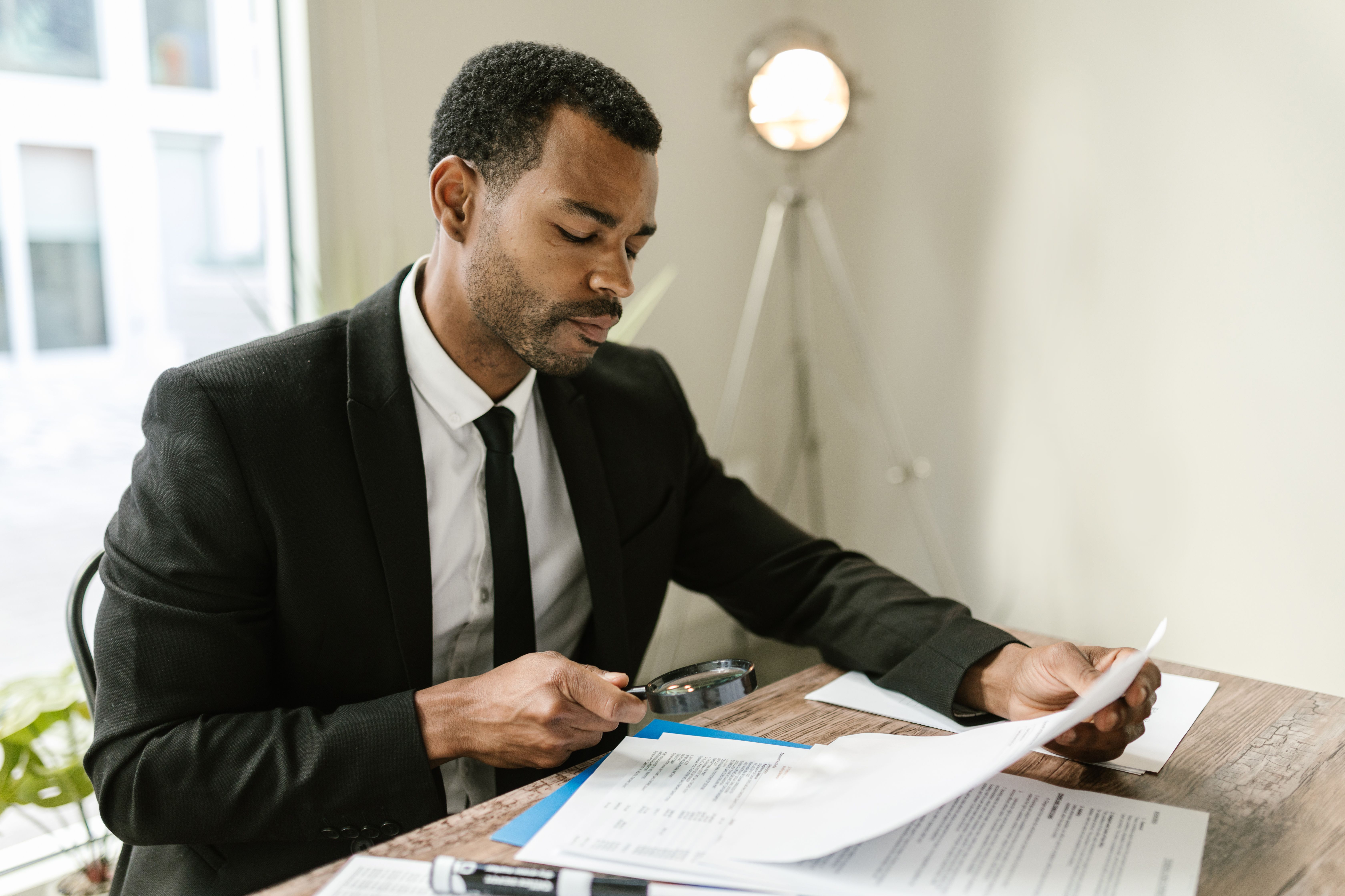 Professional examining documents with a magnifying glass to spot details in written content